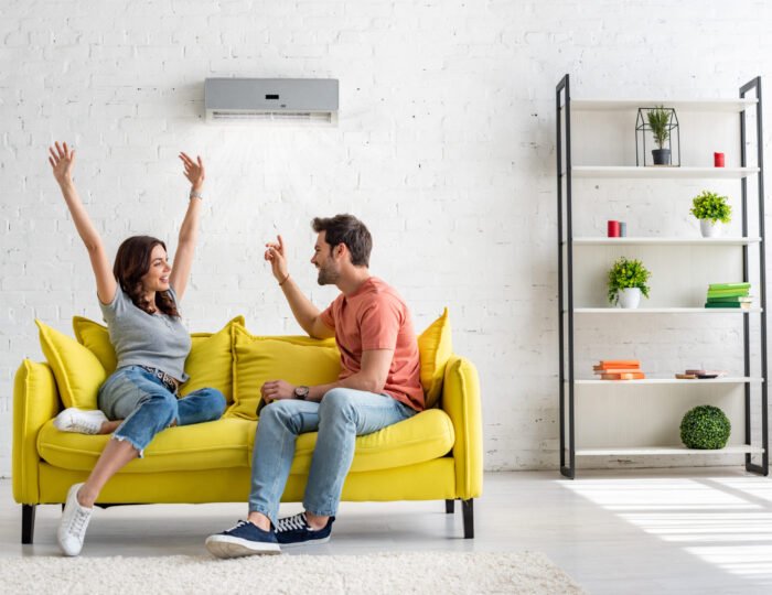 happy man and woman talking while sitting on yellow sofa under air conditioner at home happy man and woman talking while sitting on yellow sofa under air conditioner at home